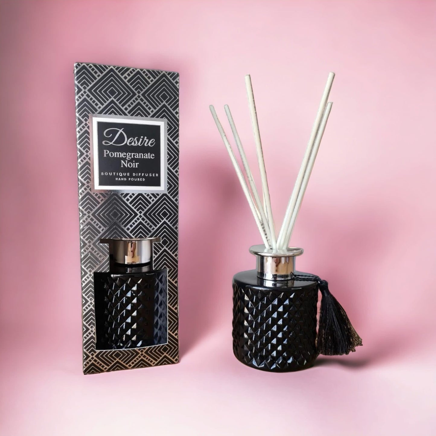 A Pomegranate Noir Reed Diffuser from The Soap Gal x, featuring exquisite design and its packaging against a pink background.