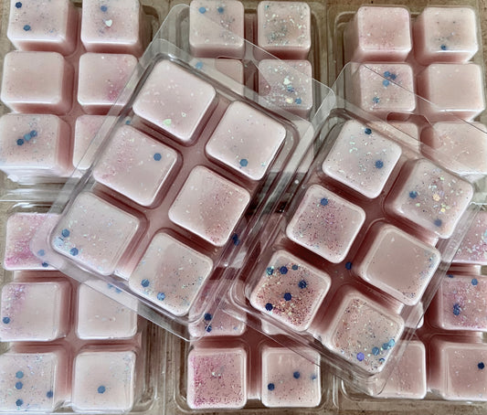 Multiple packs of Black Raspberry and Vanilla wax melts with glitter sprinkled on top arranged in rows by The Soap Gals.