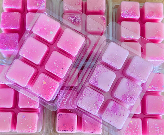 Several plastic clamshell cases filled with pink Pixie Dust Wax Melt by The Soap Gals, each divided into six cubes, are displayed in a neatly arranged manner. Some cubes have sprinkles or glitter on top, adding a touch of pixie dust.