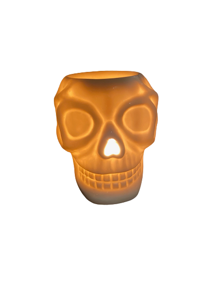 A ceramic skull candle holder with a lit candle inside glows with a warm light, perfect for adding an eerie charm to your space. This White Skeleton Plug In Wax Warmer by The Soap Gal x features an electric wax melter element, blending functionality and festivity effortlessly.