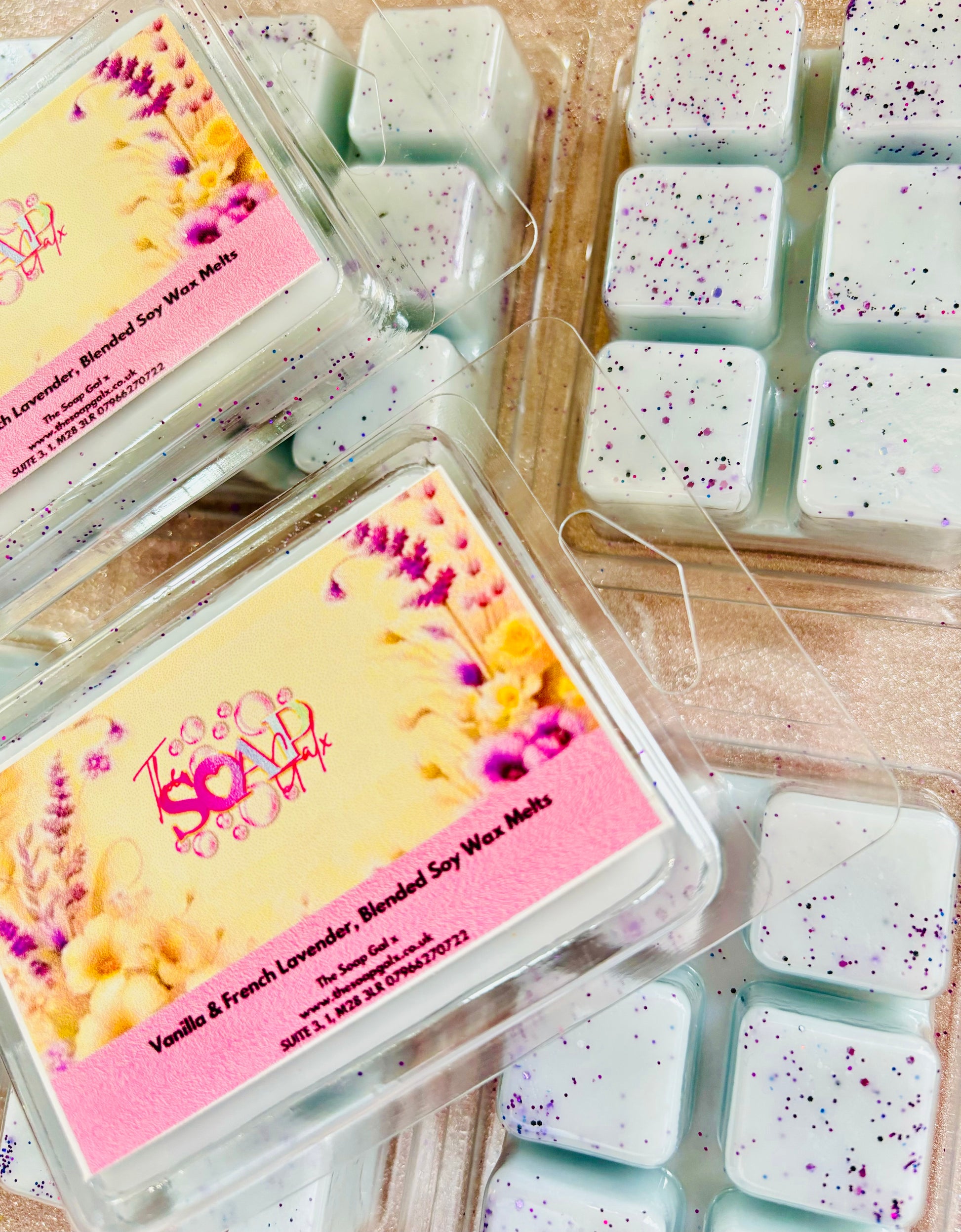 Packaged Lavender and Vanilla Wax Melts with floral design beside loose Lavender and Vanilla Wax Melts with purple speckles from The Soap Gal.