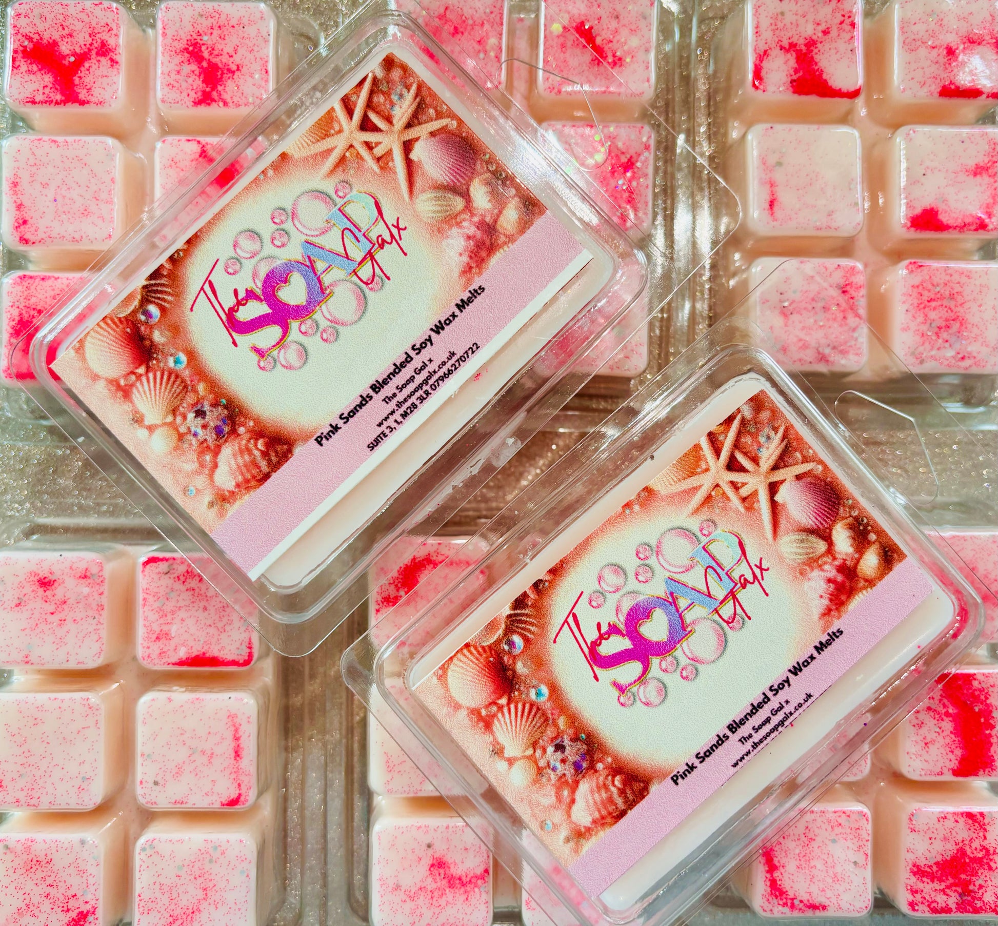 Colorful eyeshadow palettes with ocean-themed decoration displayed on a background of pink and white square textures, reminiscent of The Soap Gals Pink Sands Wax Melt Snap Bar.