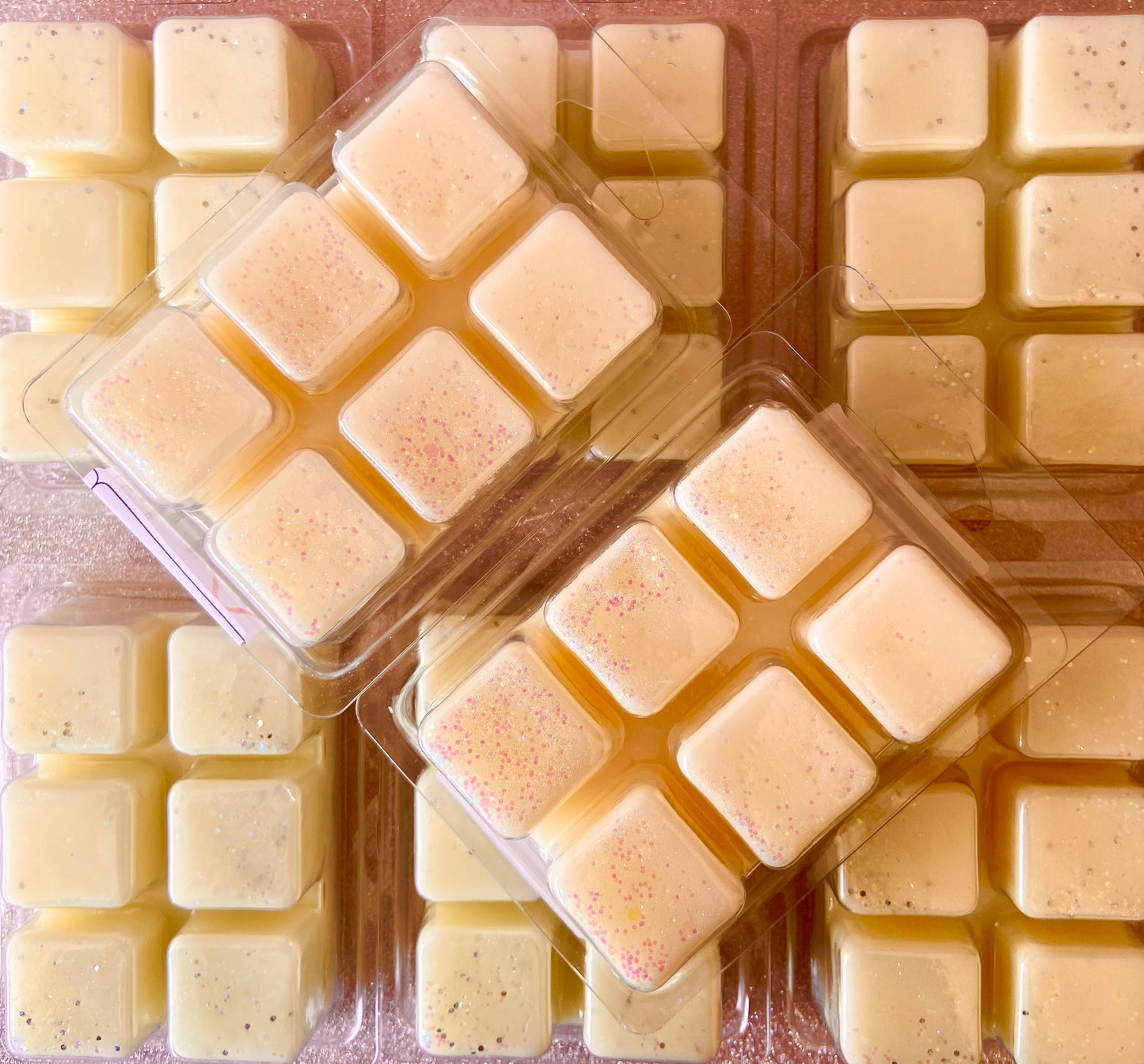 Several plastic clamshell containers each hold nine creamy white Toffee Apple Wax Melt by The Soap Gal x with scattered colored specks, arranged in a flat layout. Infused with the warm, inviting bonfire scent, these soy wax melts evoke cozy evenings by the fire.