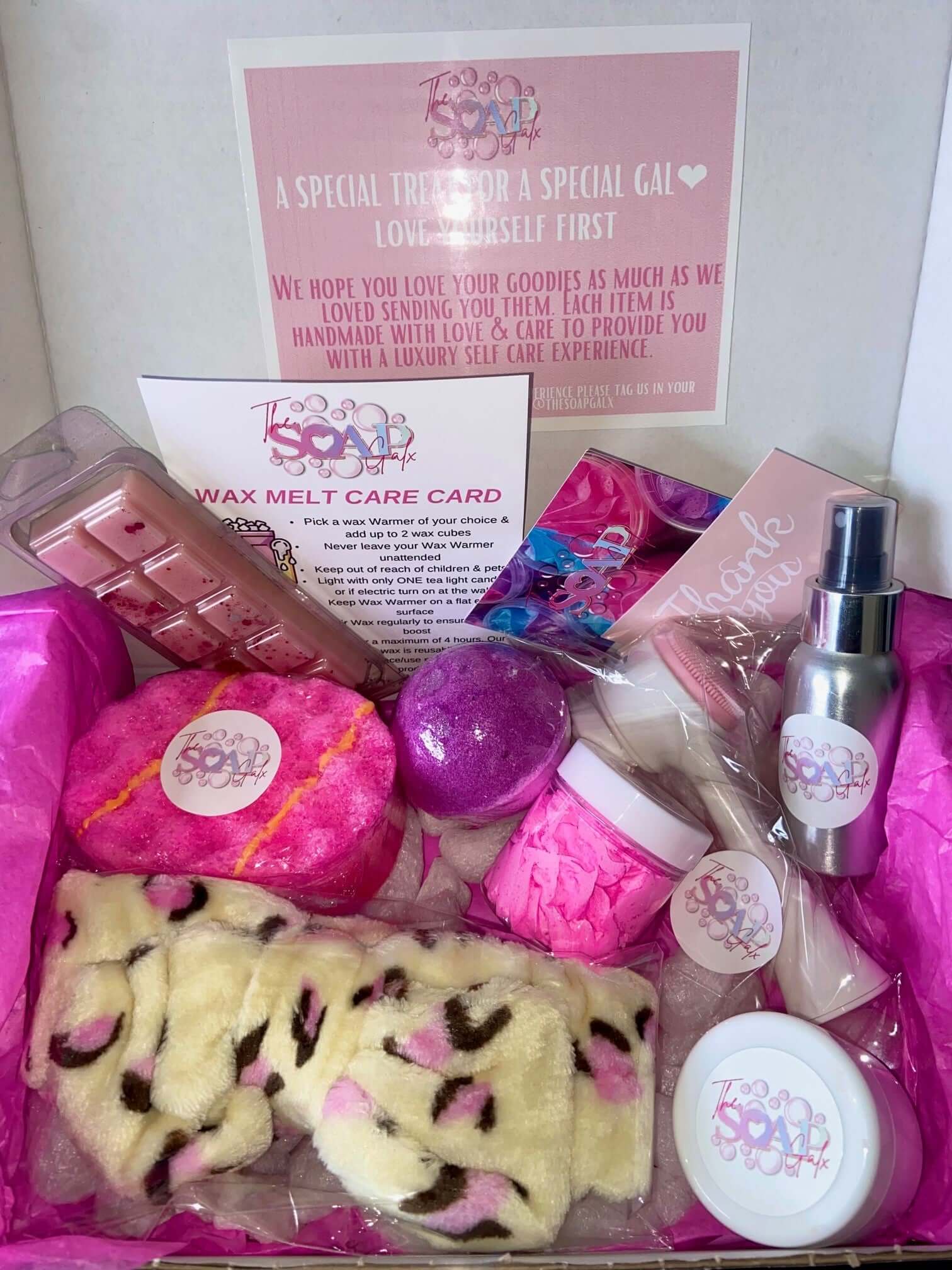 A pink Mystery Box by The Soap Gal x with a variety of skincare items inside.