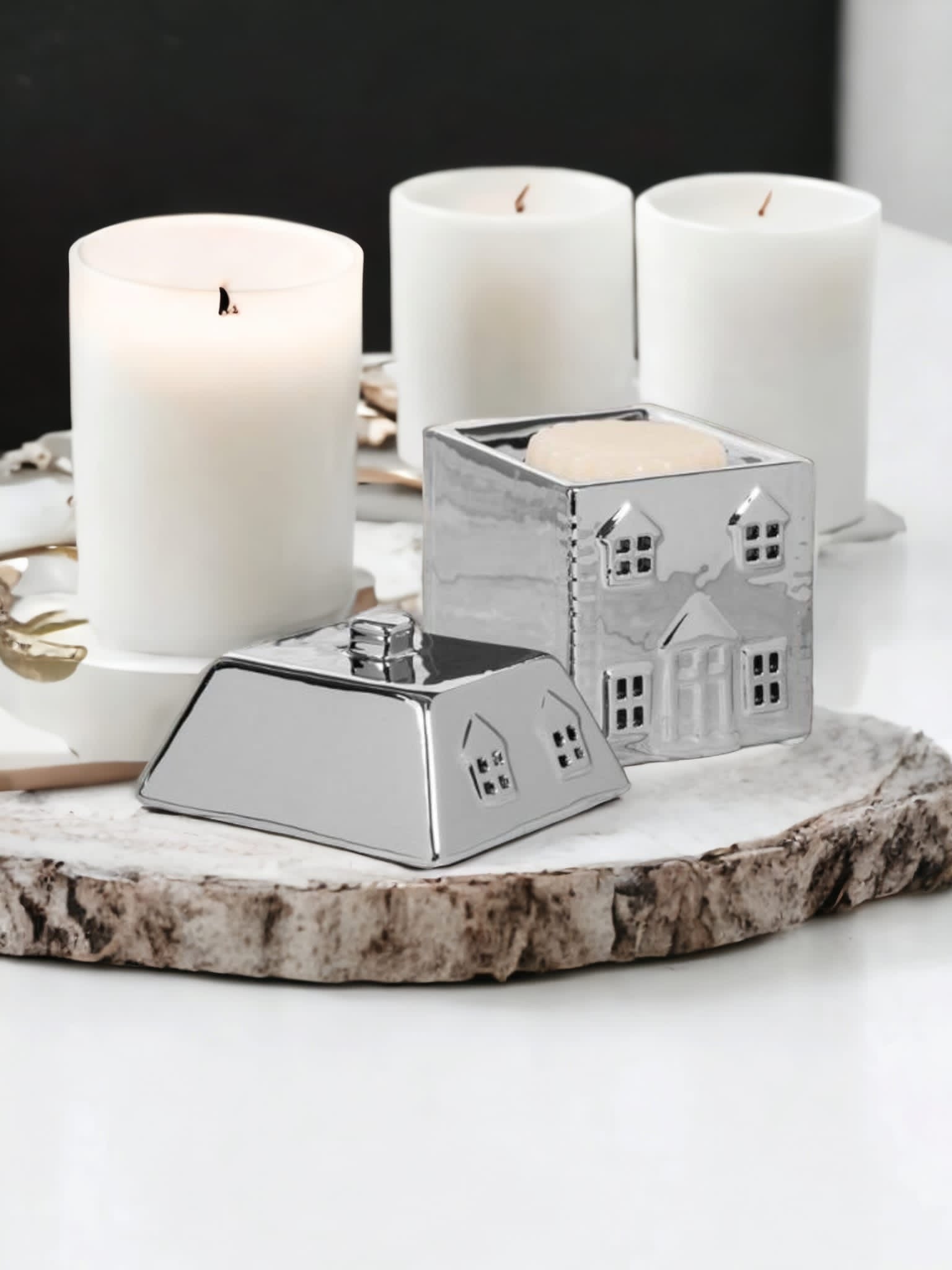 Candles and a Silver Cosy Home Wax Melt Burner by The Soap Gal x on a wooden slice against a white background.
