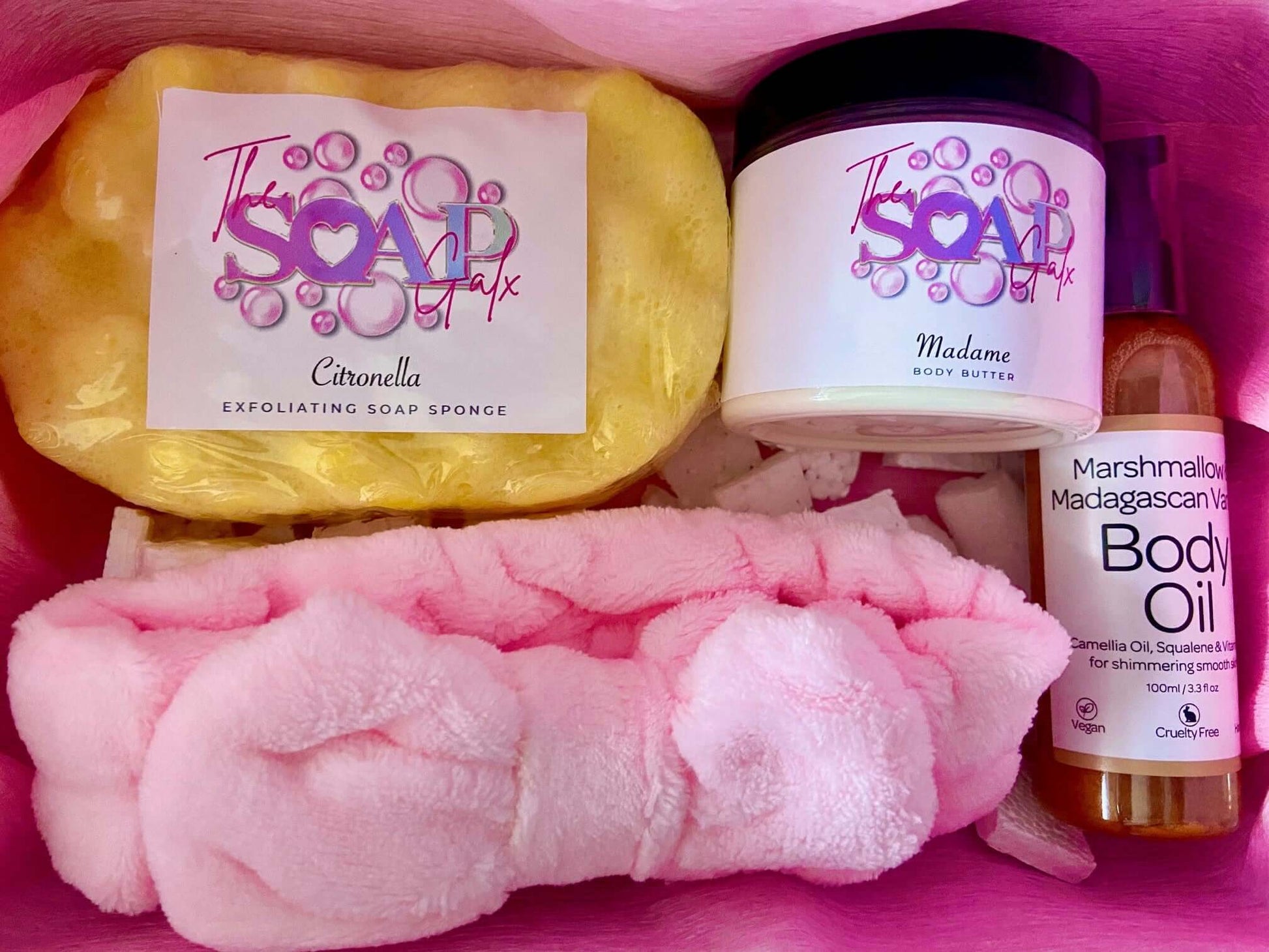 A pink Mystery Box with soap, lotion, and other skincare items from The Soap Gal x.