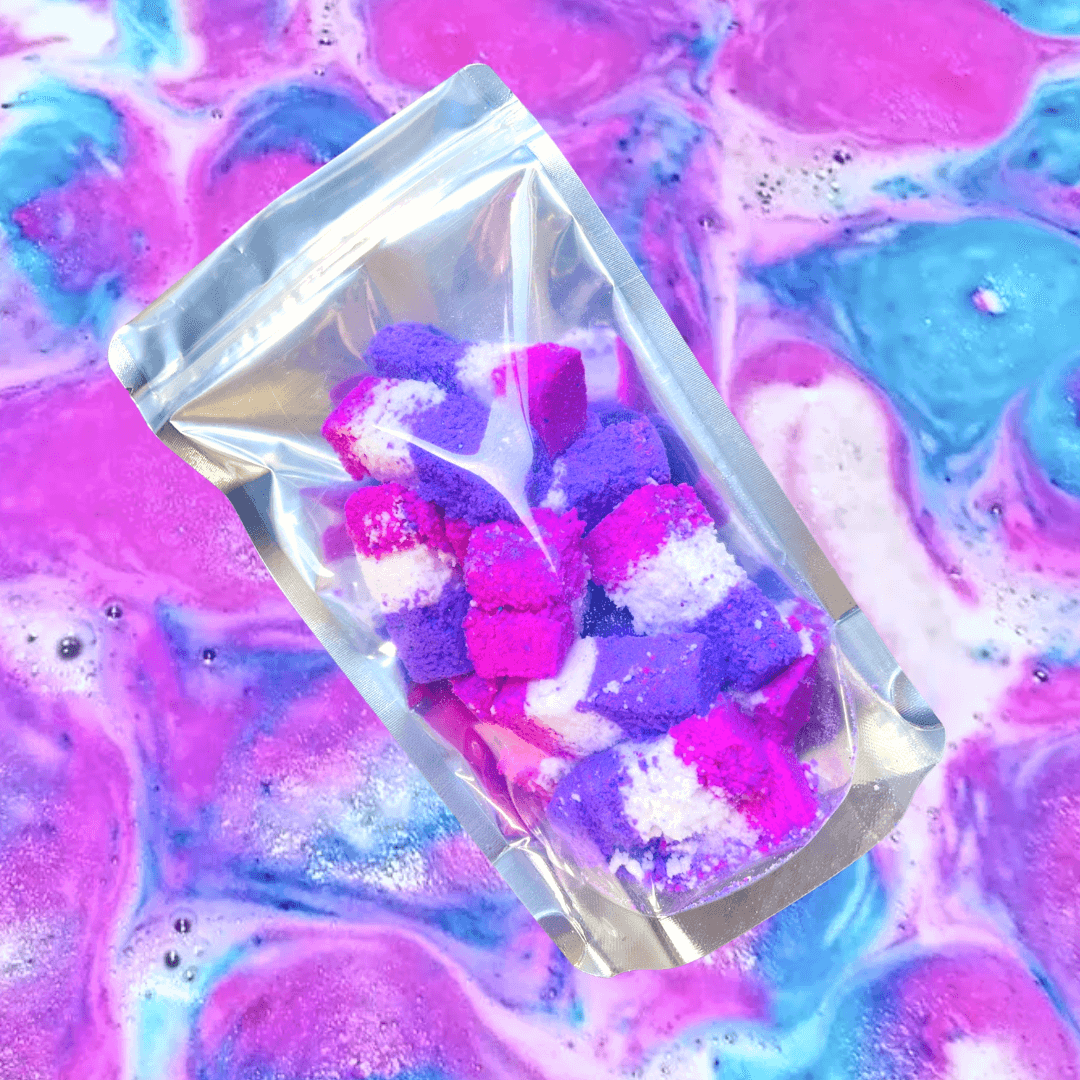A bag of pink and purple handmade Bath Rocks Bath Bombs from The Soap Gal x sitting on top of a colorful background.