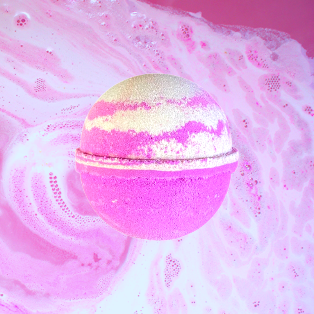 A pink The Soap Gals Drumstick Lolly Bath Bomb with white and gold accents floating on sudsy water, creating vibrant swirls around it.