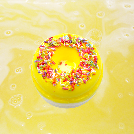 A Lemon Meringue Bath Bomb from The Soap Gals floating on a liquid surface with ripples.