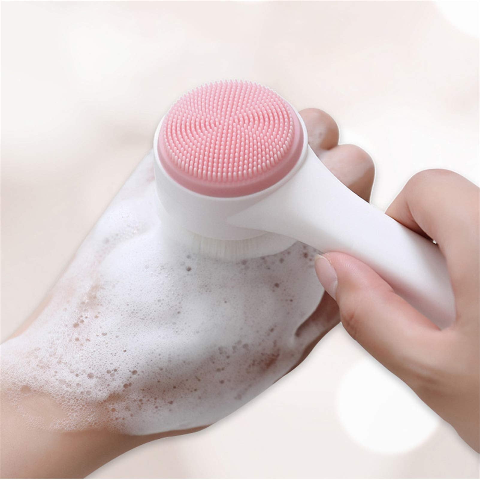A hand holding a pink Exfoliating Face Brush from The Soap Gal x with soap foam on a white background.