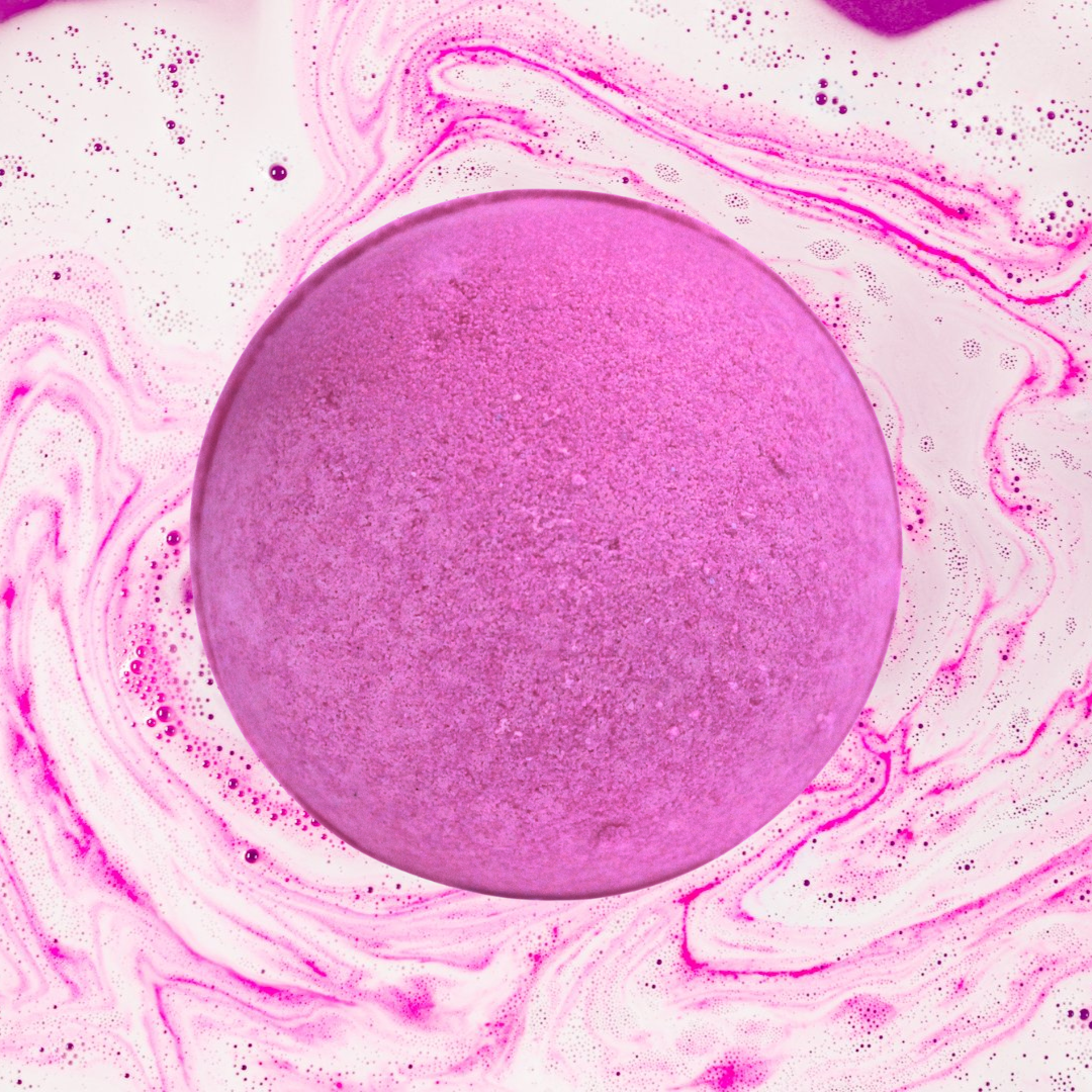A pink spherical Party Girl Perfume Jumbo Bath Bomb by The Soap Gal x surrounded by swirls and patterns in shades of pink.