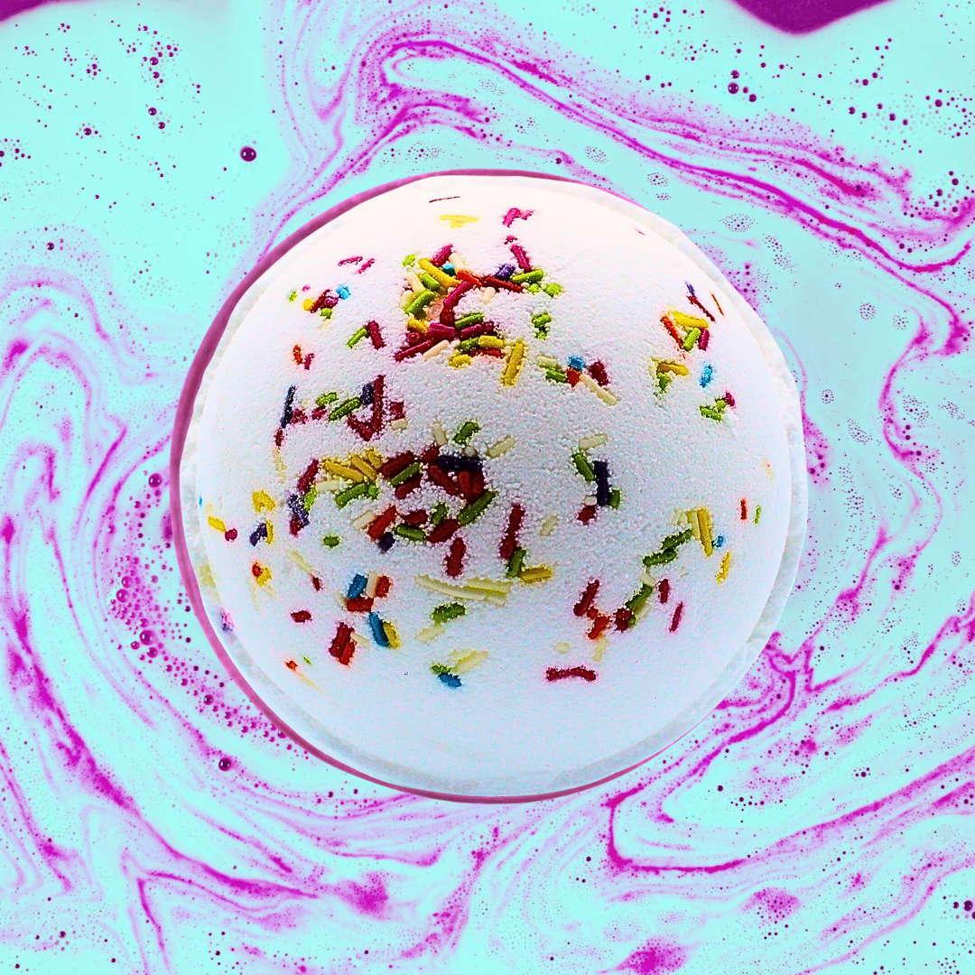 A Rainbow Sprinkles Jumbo Bath Bomb from The Soap Gal x dissolving in water, releasing colorful streaks.