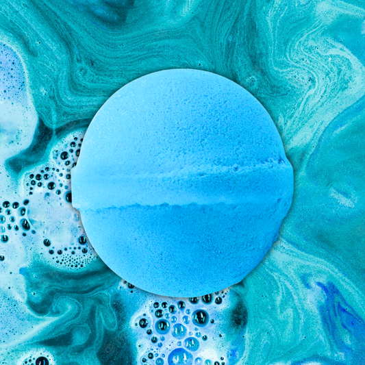 A blue Texas Dewberry Jumbo Bath Bomb from The Soap Gal x dissolving in water, creating swirls of blue and green with bubbles.