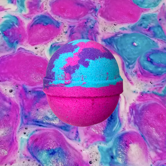 A vibrant pink, purple, and blue "Unicorn Kisses Bath Bomb" from The Soap Gals against a colorful swirling background of similar hues. This sweet edible smelling accord is suitable for vegans, adding a touch of magic to your bath time experience.